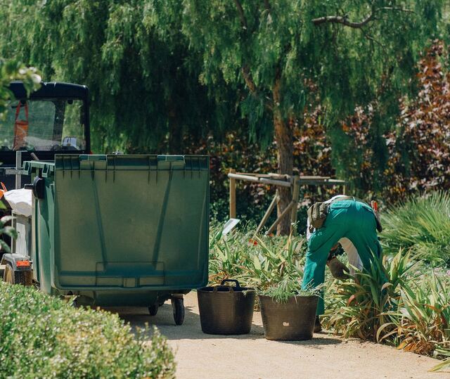 Een tuinman in werkkledij plant nieuwe planten in een border
