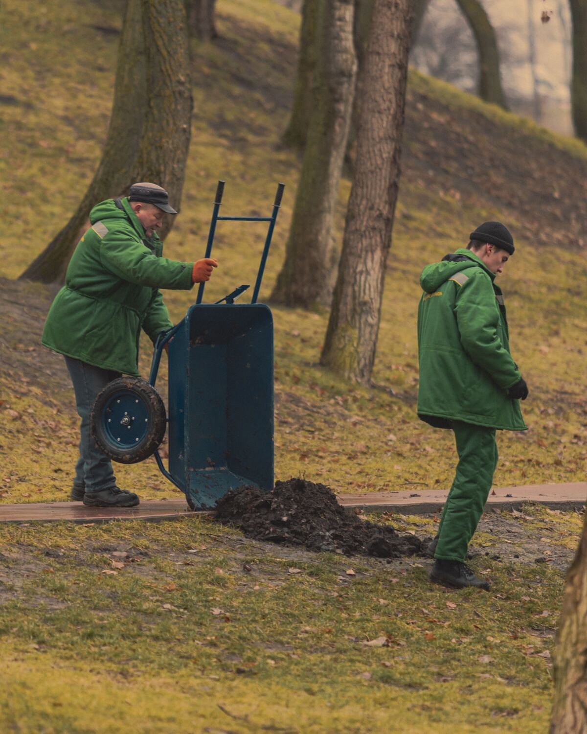 Twee tuinmannen in werkkledij lossen een kruiwagen aarde